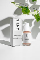 SILNT Peptide Serum bottle beside its carton with soft leaf shadows