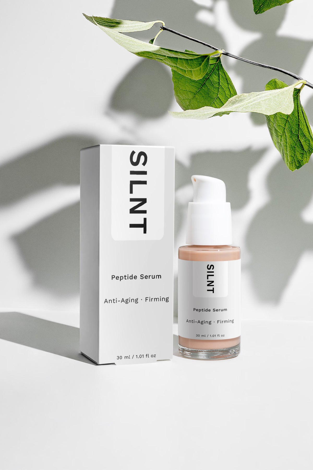 SILNT Peptide Serum bottle beside its carton with soft leaf shadows